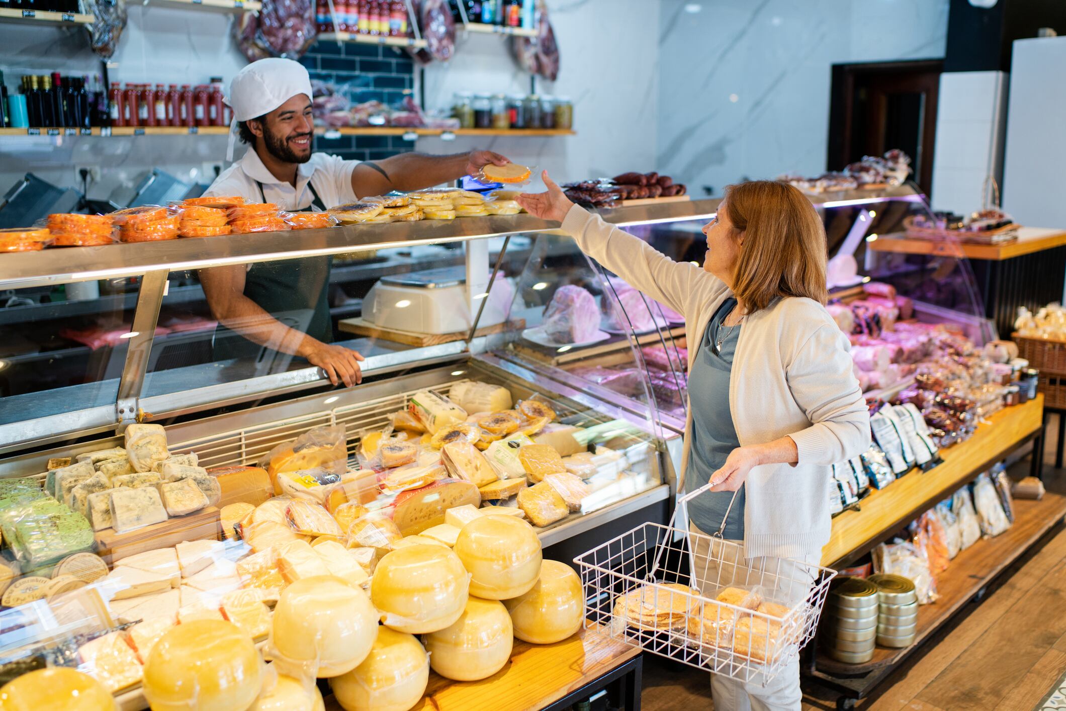 Senior woman buying cheese at grocery store. Shopkeeper serving a customer in a delicatessen.