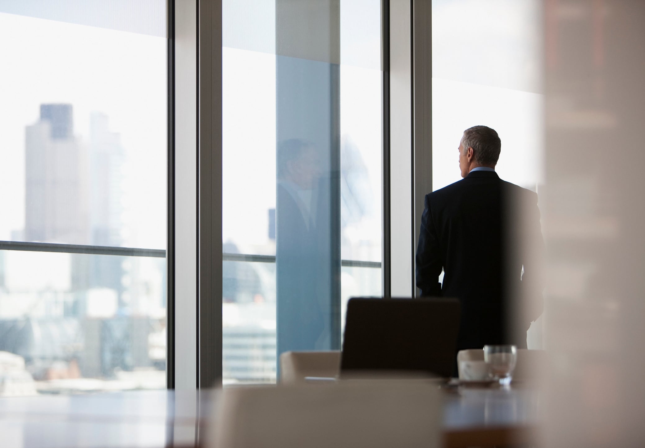 Businessman looking out conference room window Tom Merton GettyImages
