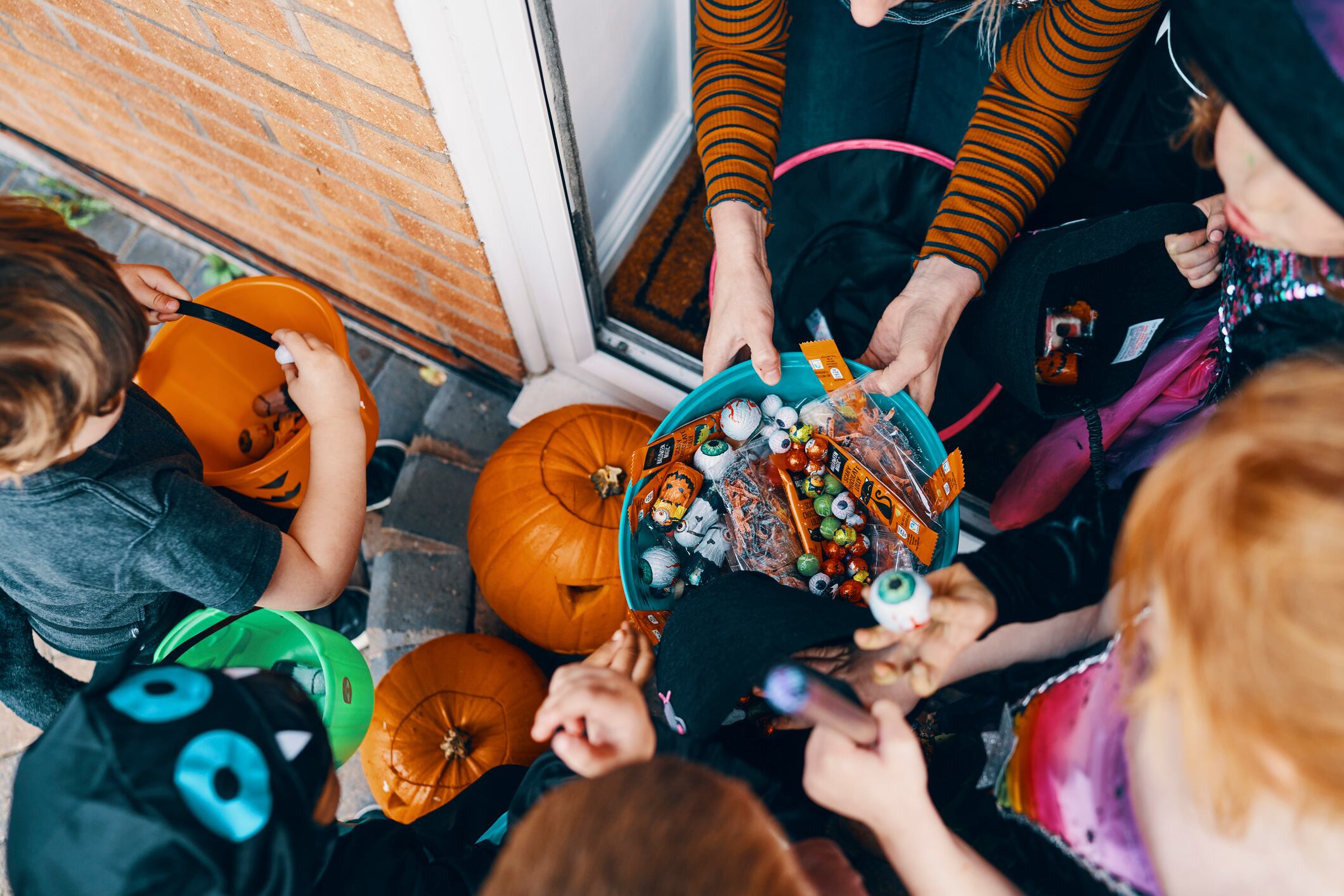 An overhead shot of kids in Halloween costumes trick or treating on a doorstep with a bucket of candy.