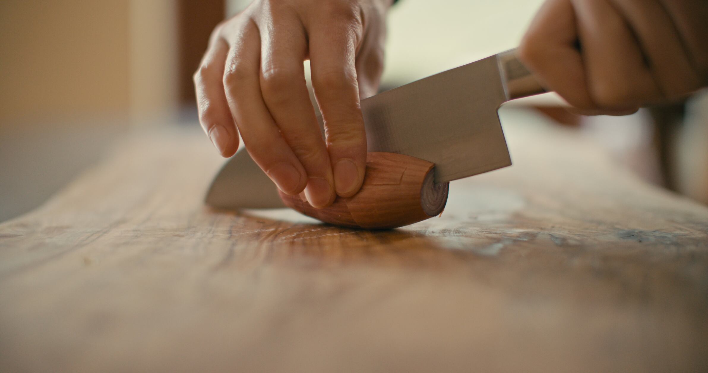 A close-up view of a hand slicing a shallot on a wooden chopping board.