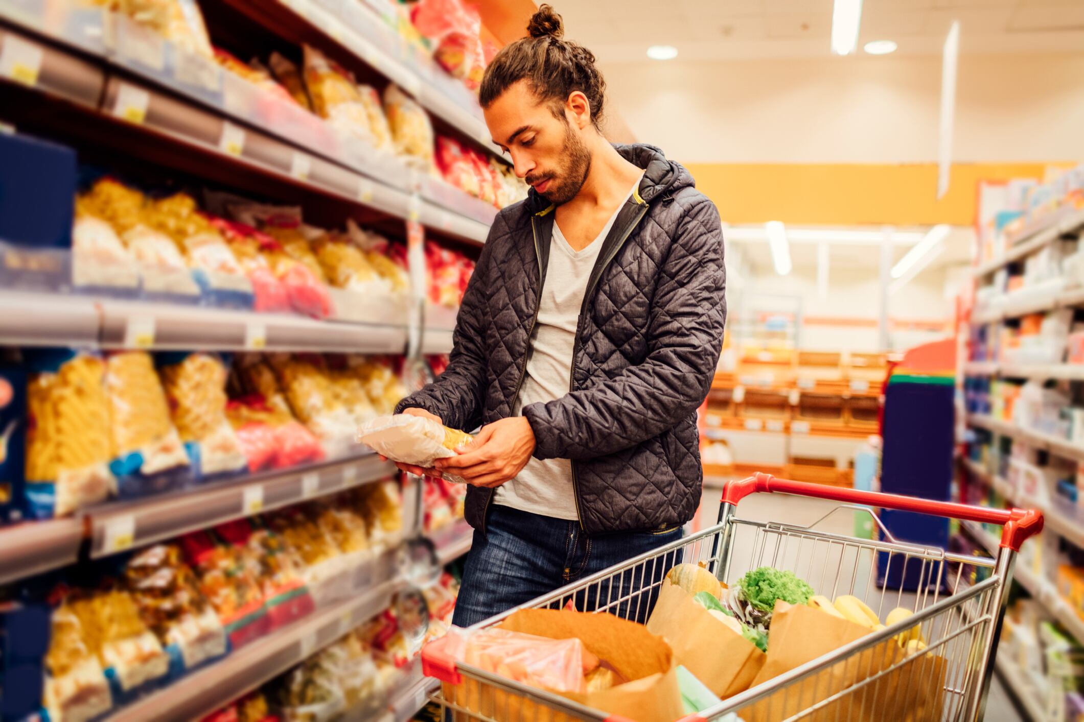 How can retailers make manufacturers label with Nutri-score: Image: Young bearded man in groceries shopping. He is choosing pasta and reading nutrition label on product. Location released.