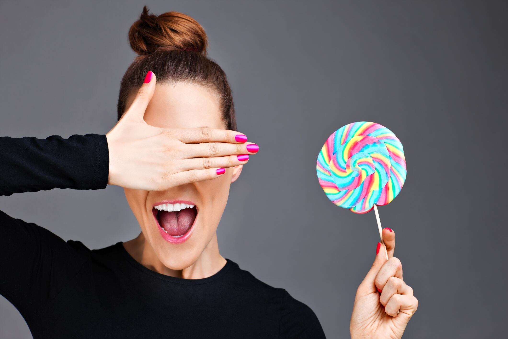 Woman holding a lollipop and covering her eyes. Gray background
