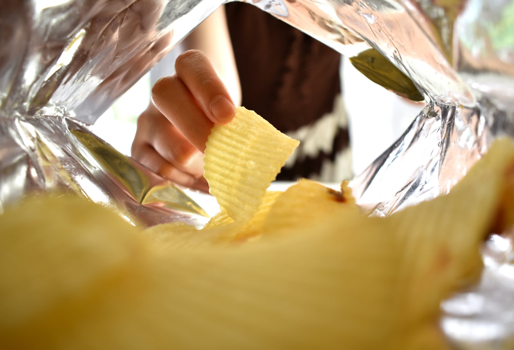 Woman's hand picking up yellow potato chips inside a bag of snacks.
