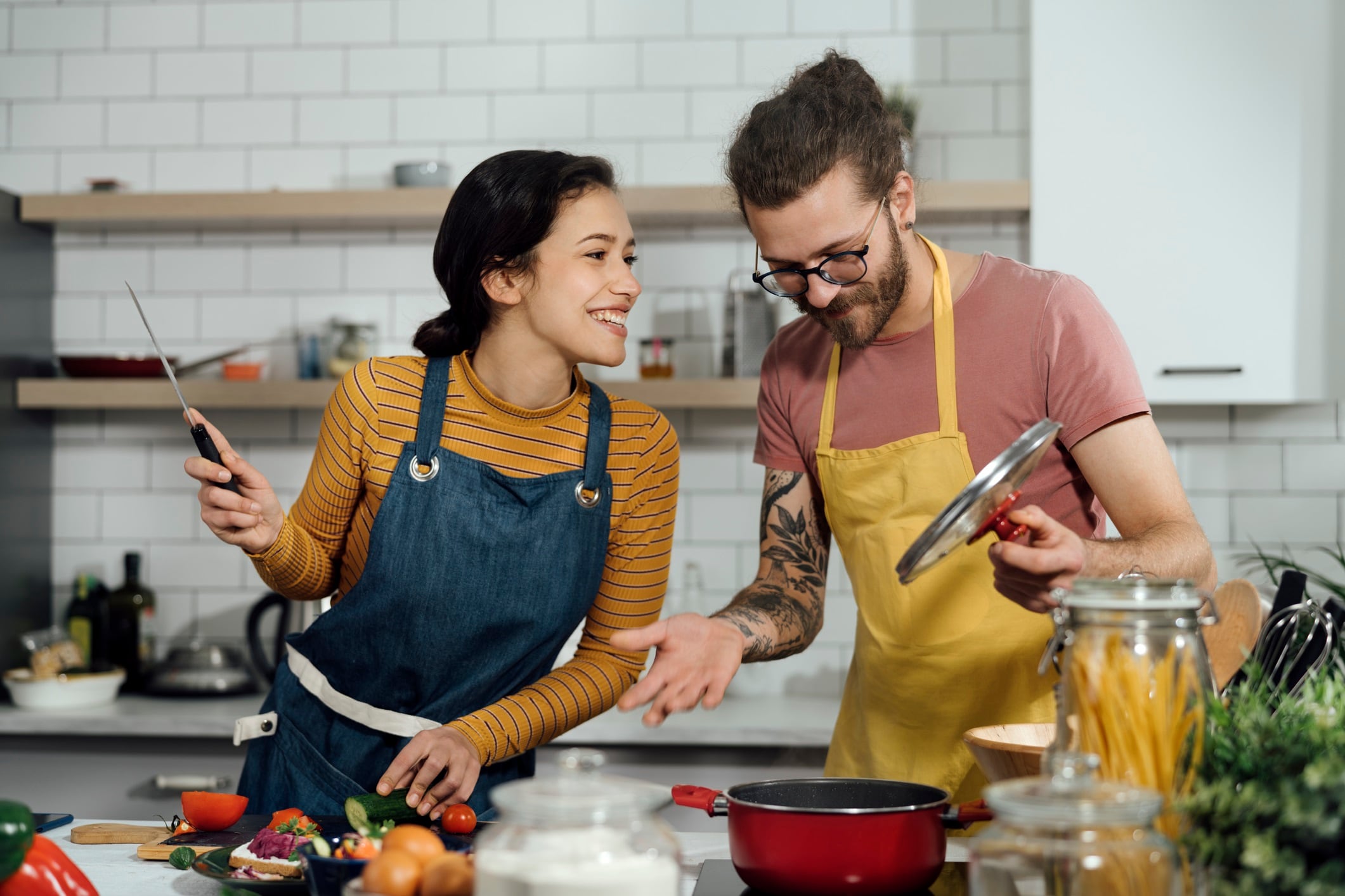 Man and woman laughing as they cook dinner in home kitchen.