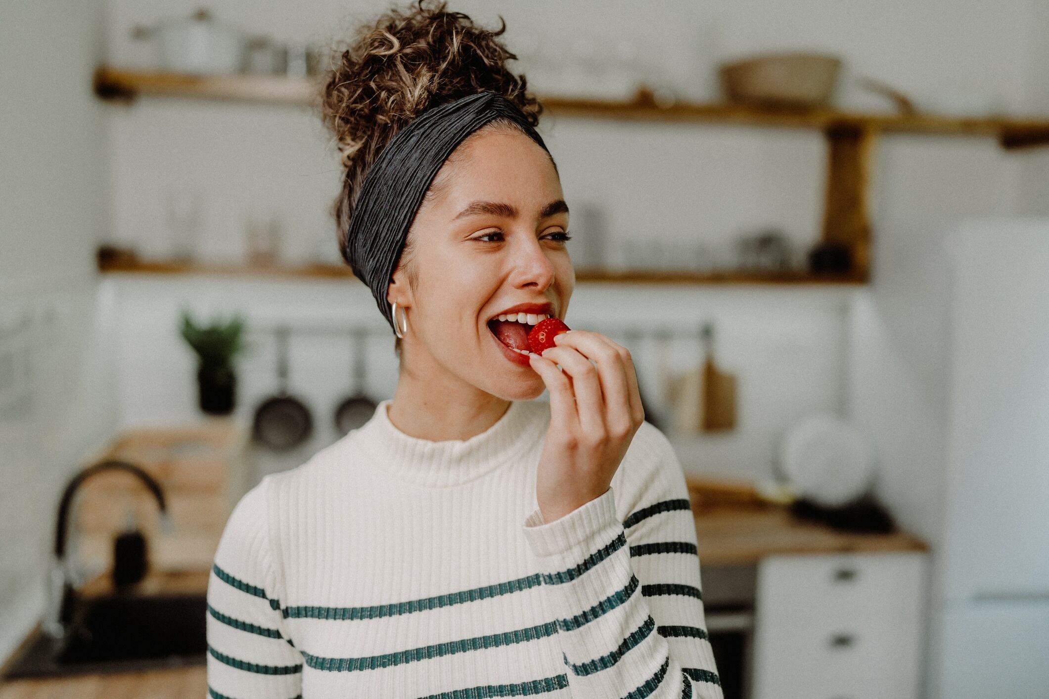 Woman eating strawberry. She's wearing a black and white stripped jumper and has her hair tied up.