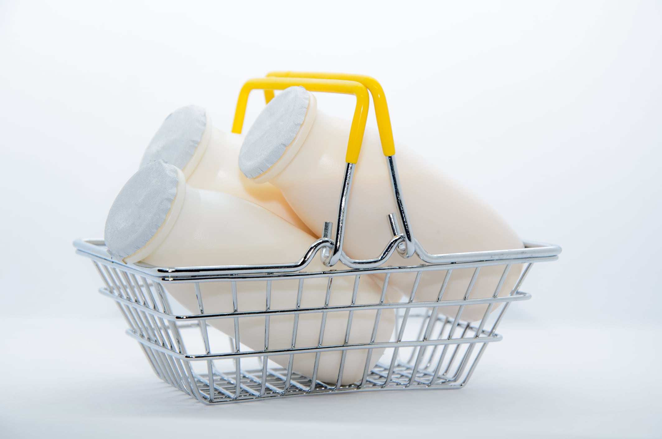 Natural yogurt with probiotics and Lactobacillus in small plastic bottles in metal shopping basket on white background. Healthy diet food, dairy products, go grocery shopping