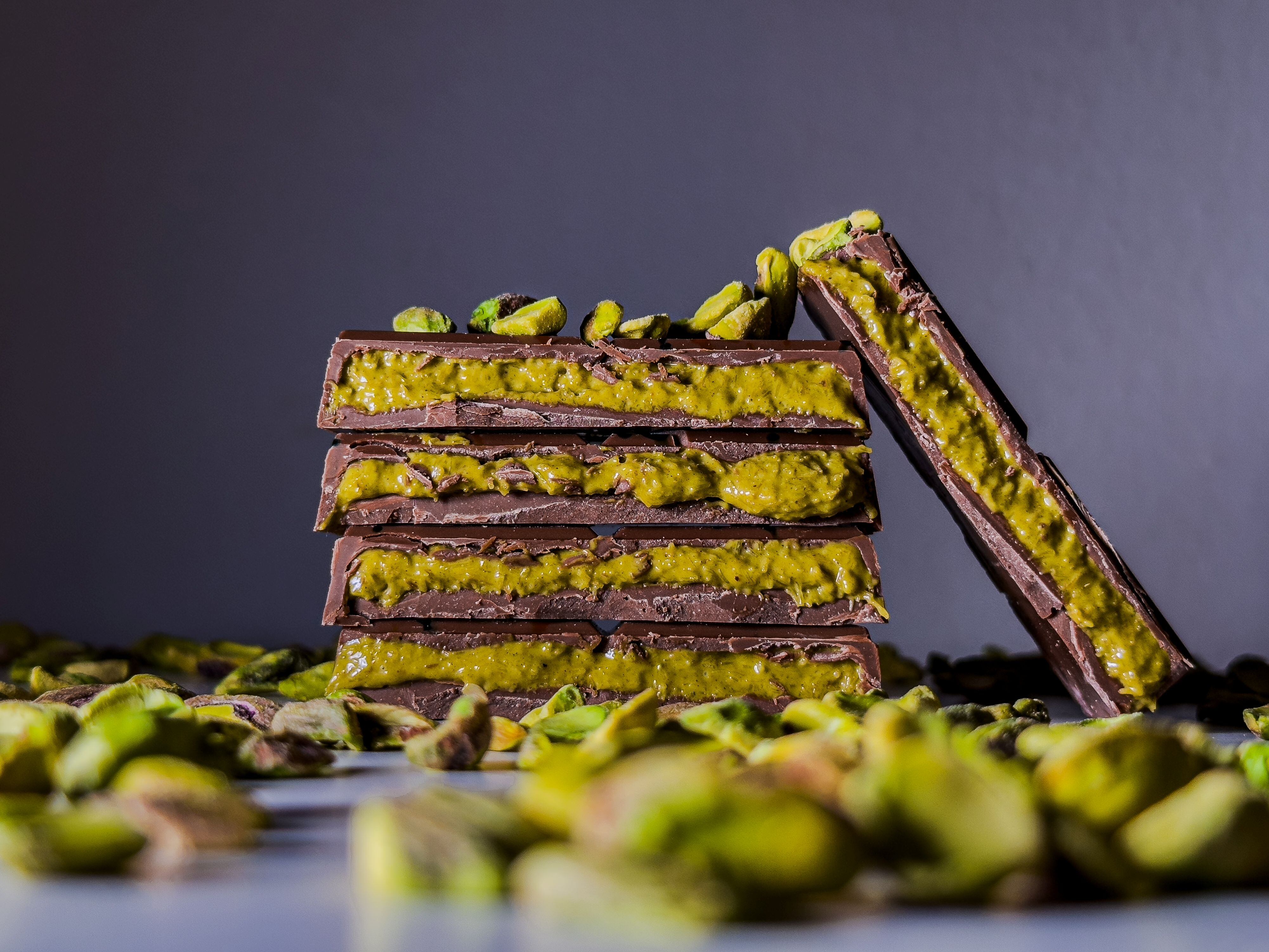 Slices of Dubai chocolate which shows the bright green pistachio and knafeh filling as well as pistachios in the foreground.