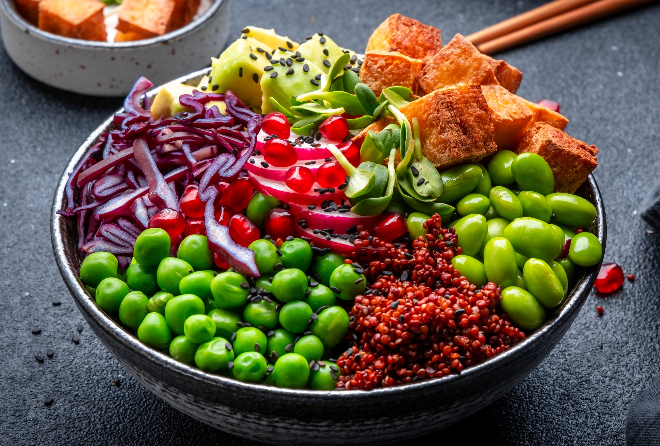 Vegan Buddha Bowl for balanced diet with roasted tofu, red quinoa, vegetables, legumes, seeds and sprouts. Black table background, top view