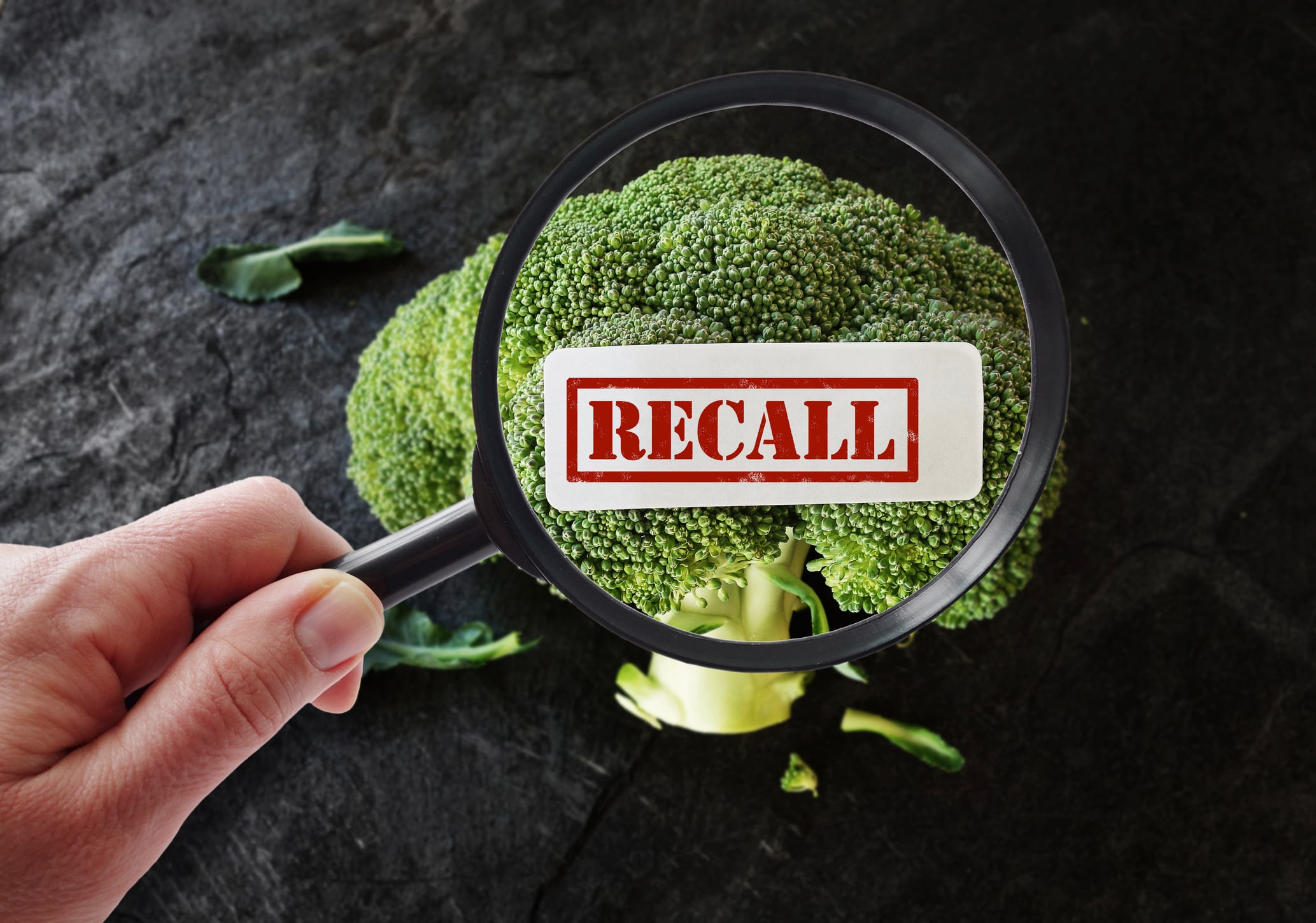 Hand with magnifying glass looking at broccoli Recall label