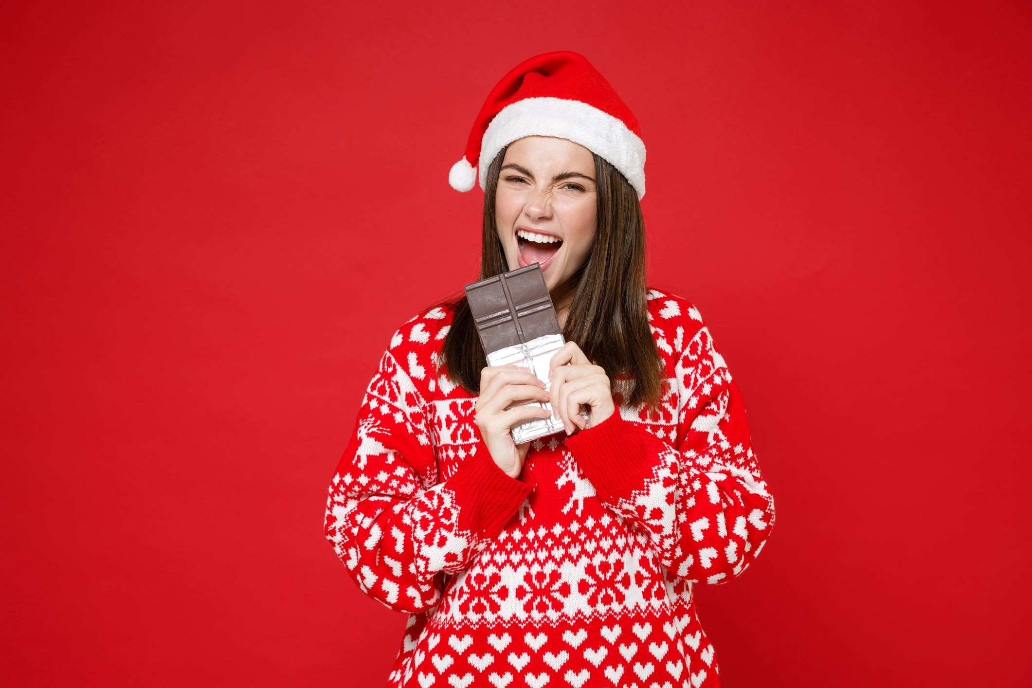 Woman wearing Christmas jumper and hat, and eating chocolate