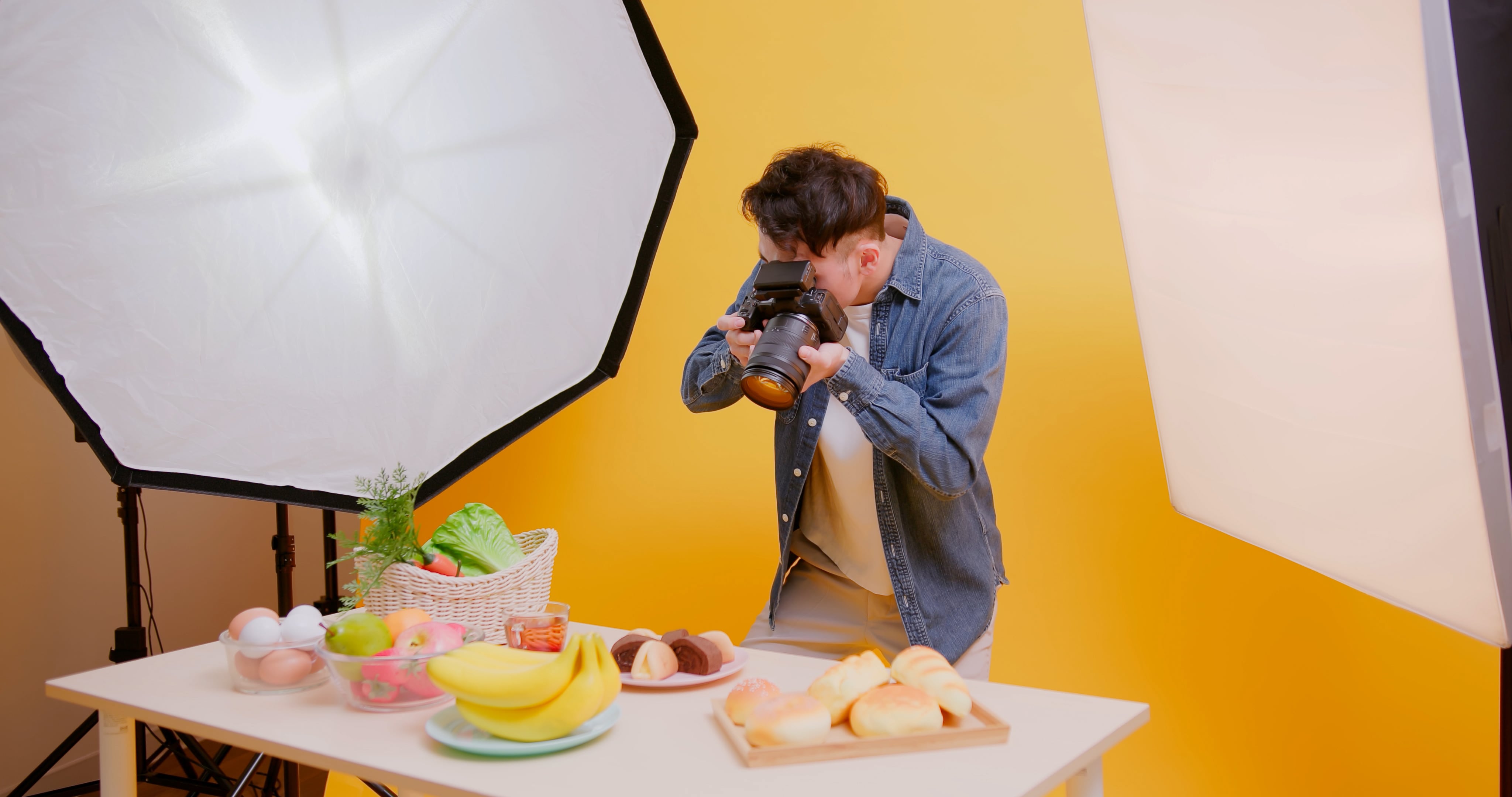 asian young male photographer use professional camera shooting food in front of yellow background at studio