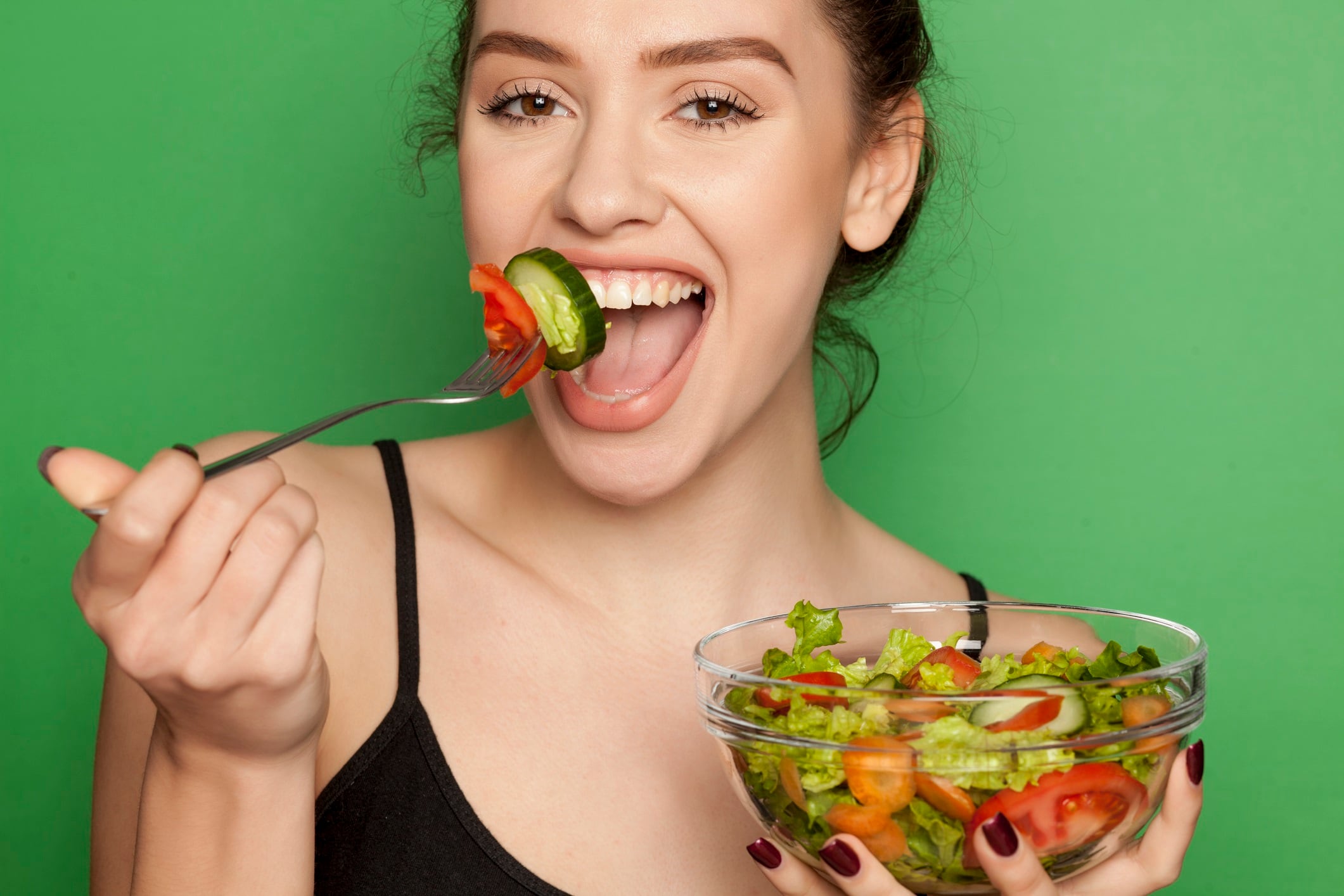 Young beautiful woman eating salad on green background