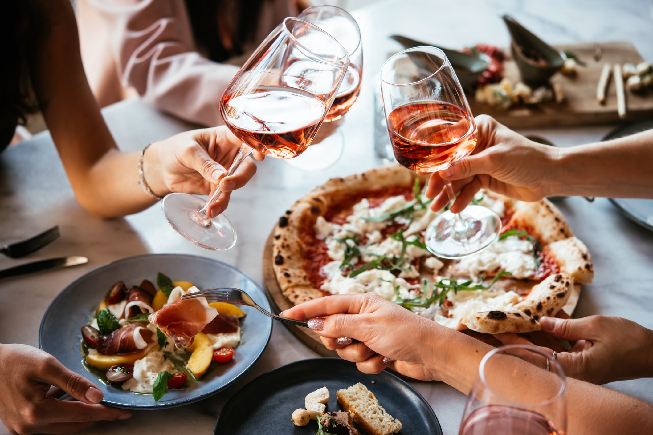 Friends enjoy a dinner party with pizza and rose wine in a bar or a restaurant.