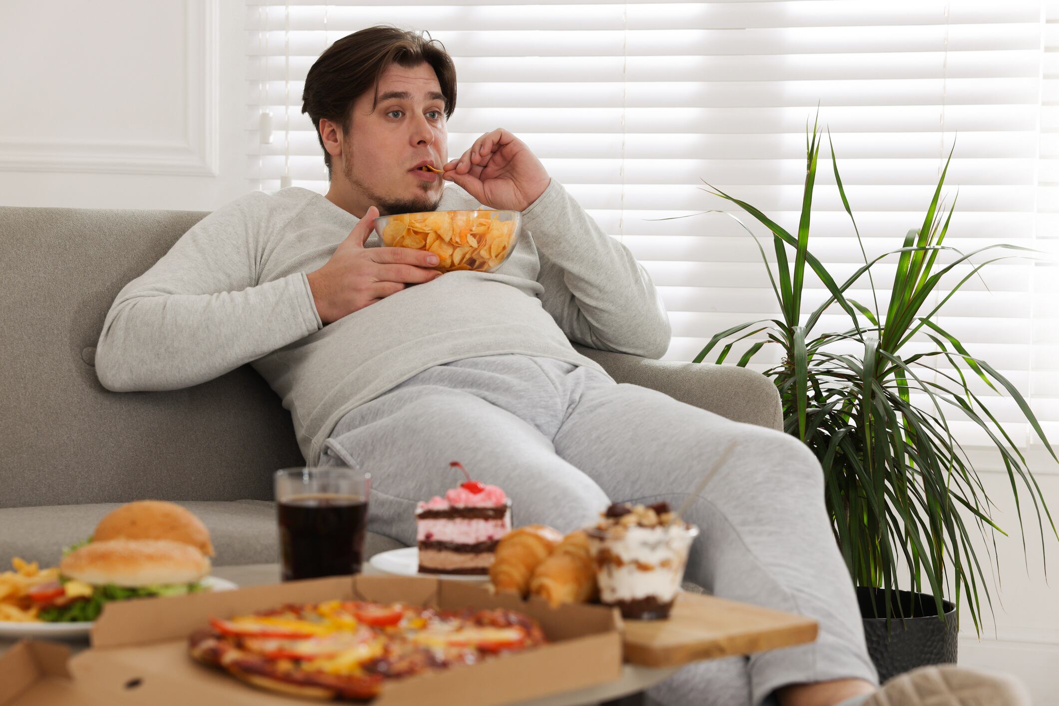 Overweight man with chips on sofa at home