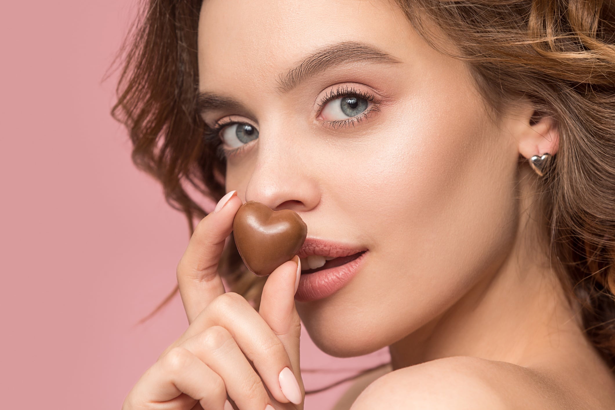 Woman holding heart-shaped chocolate. Pink background.