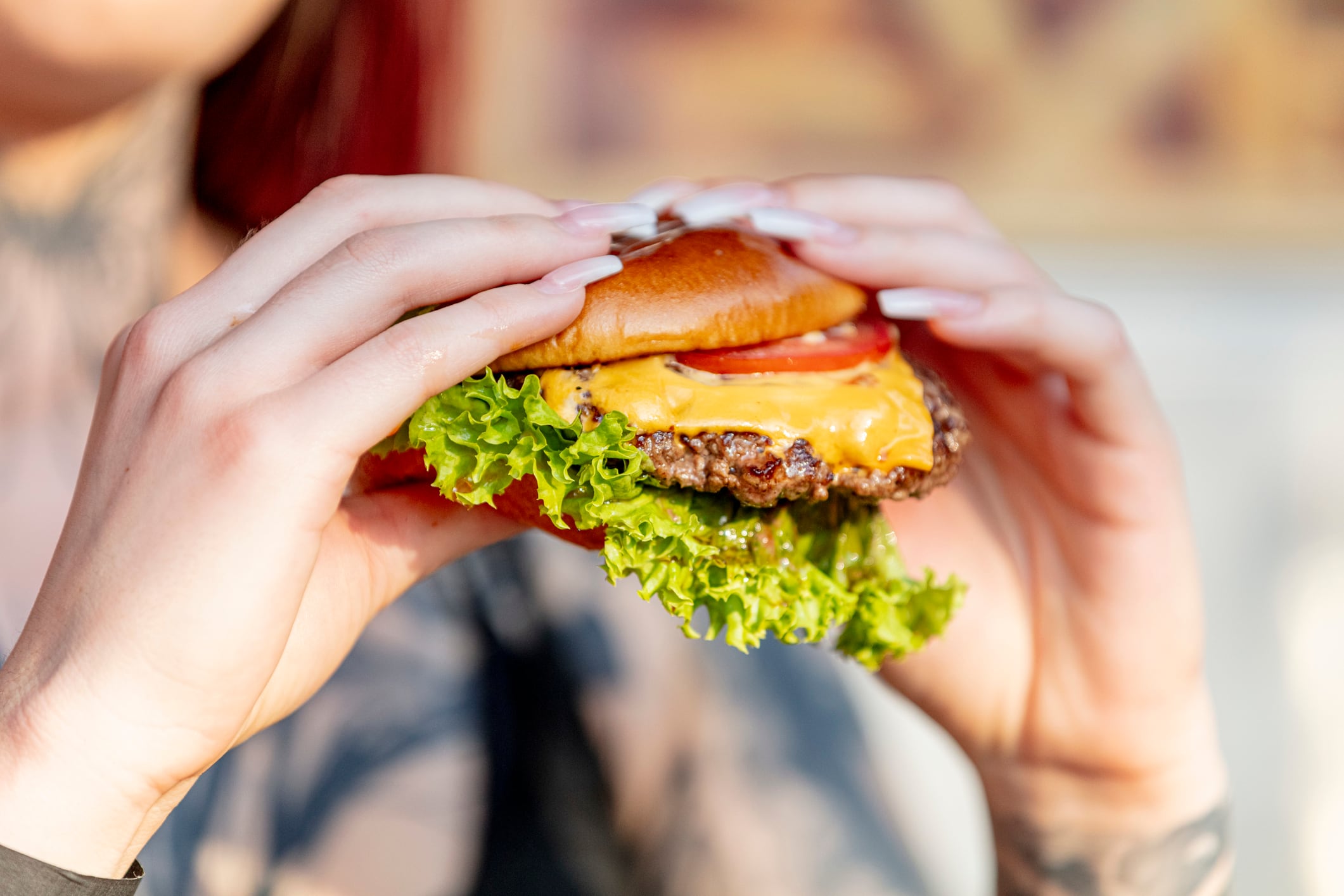 Woman holds freshly made cheeseburger outdoors in the summer sun.