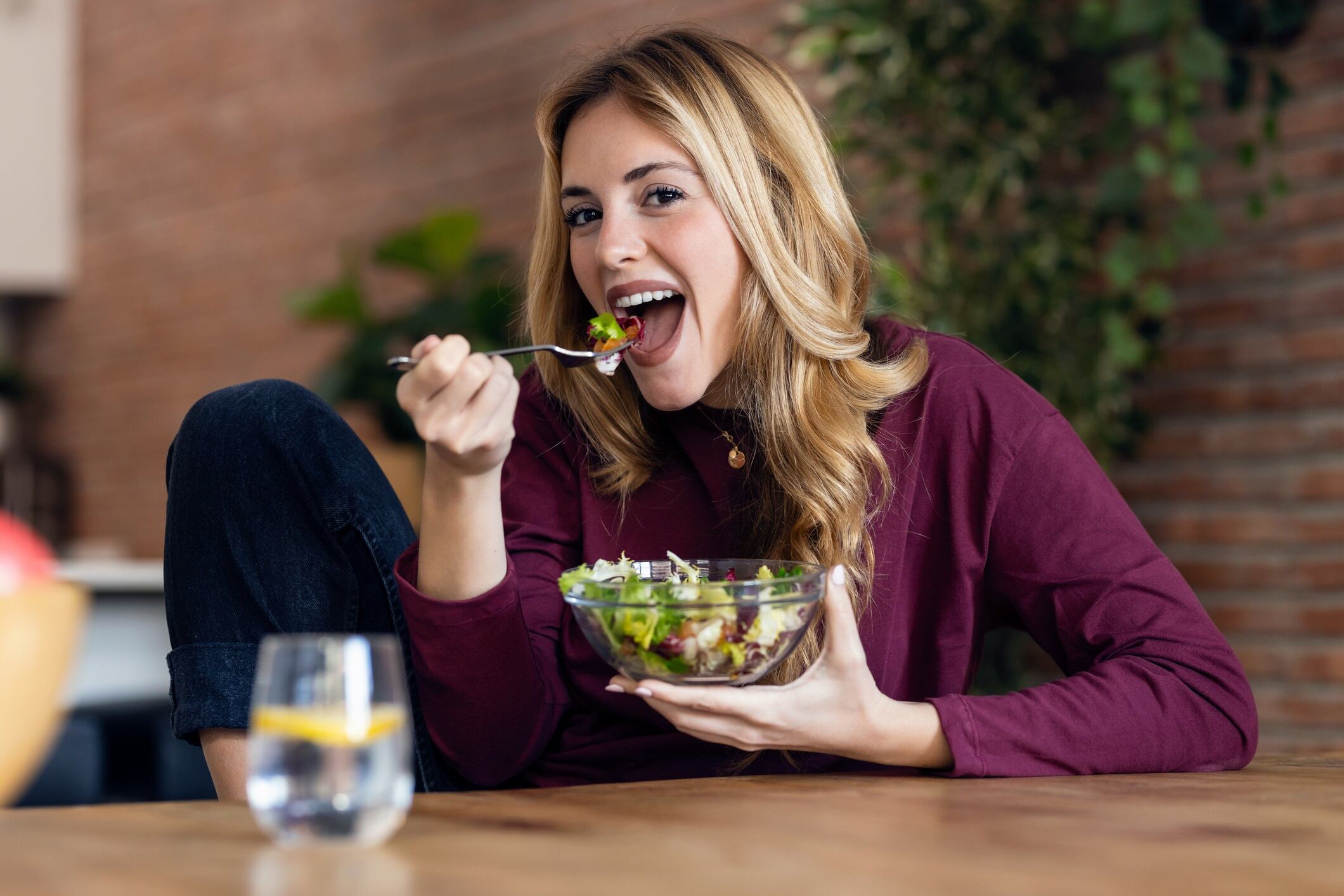 Shot of smiling woman eating healthy salad while sitting in the kitchen at home.