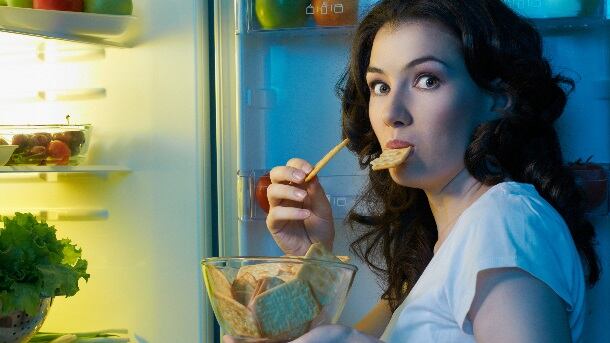 Woman eating crackers in front of open fridge