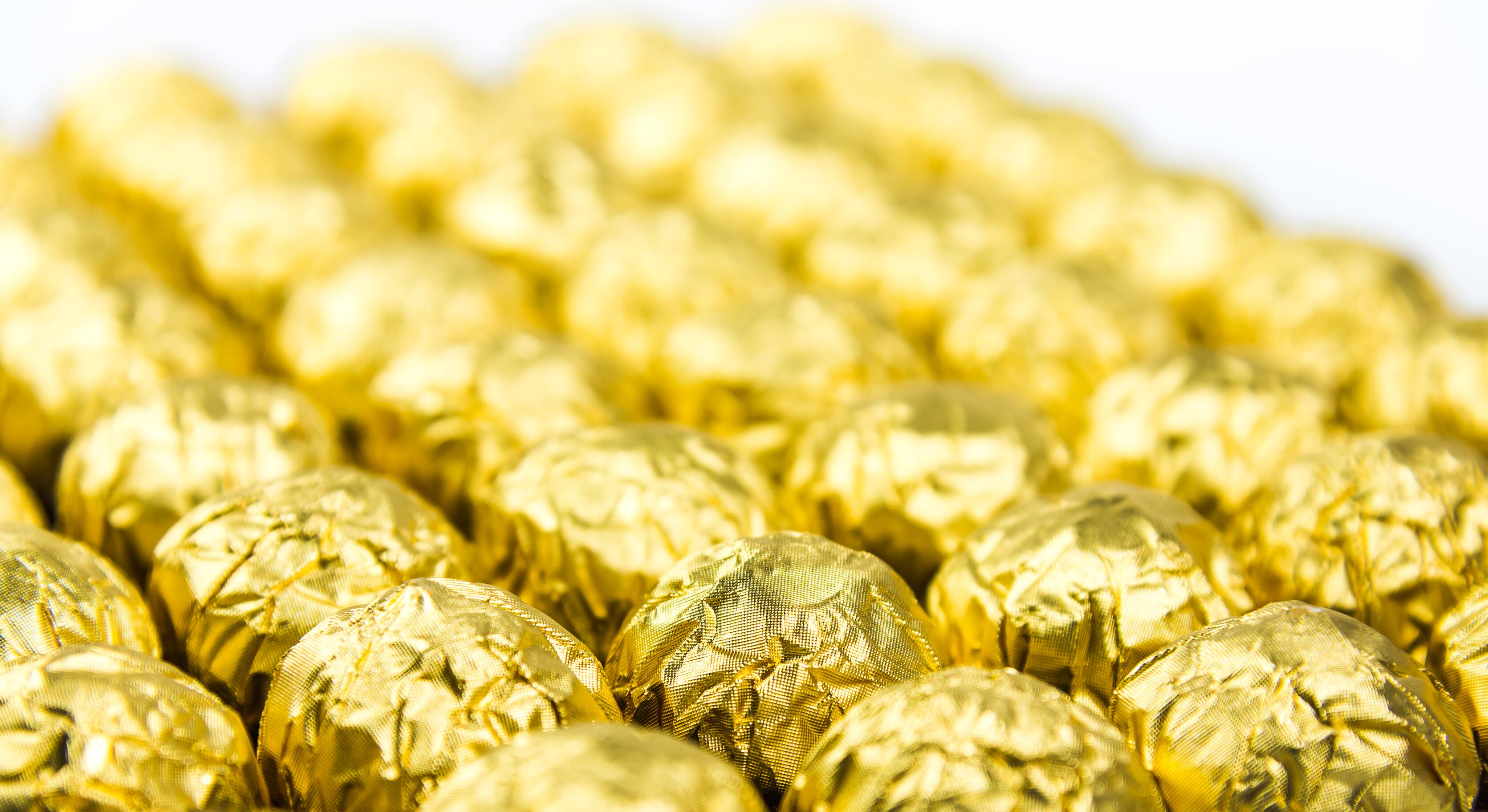 a lot of shiny golden chocolate wrapper in line on white background..