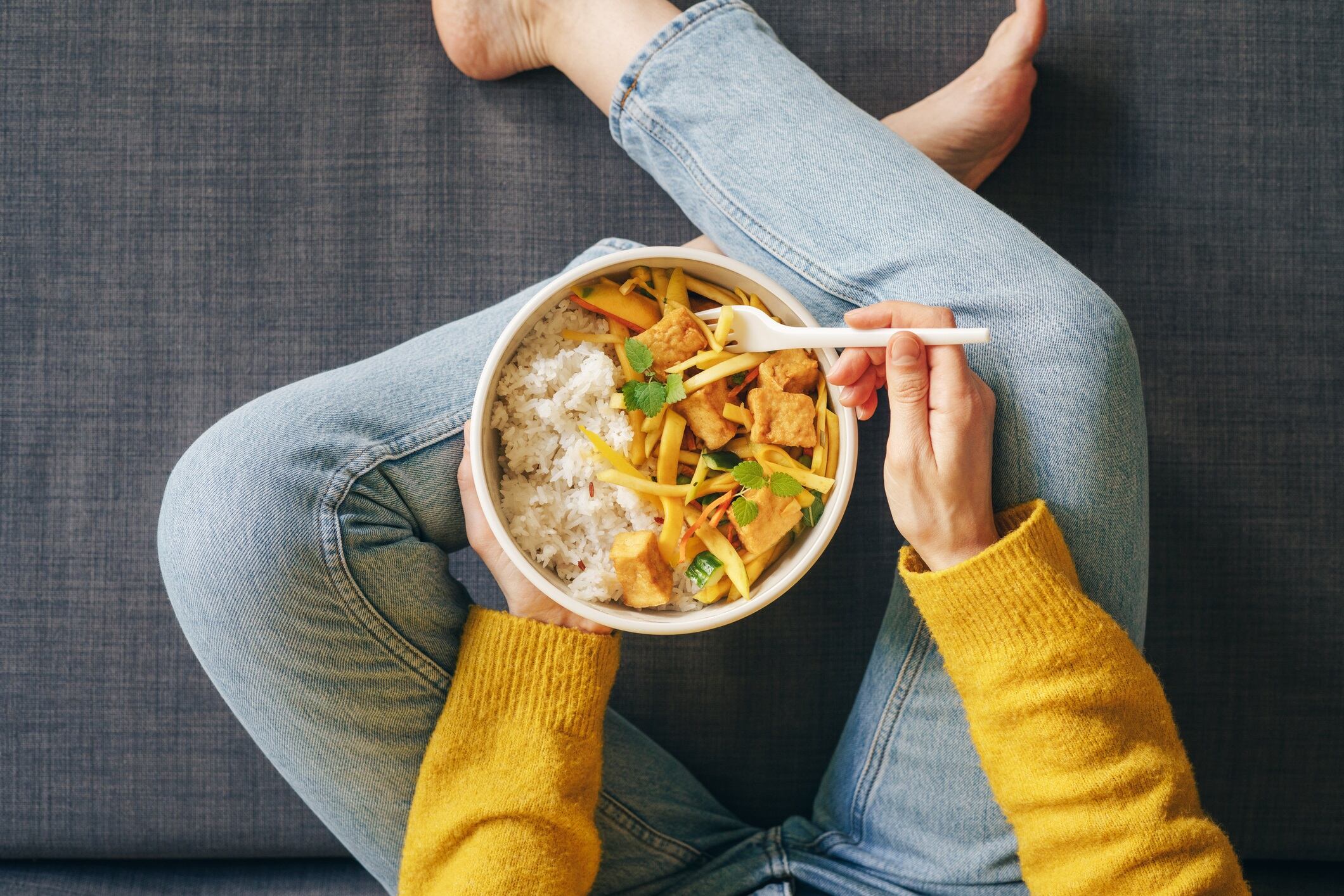 Woman sat on floor, eating rice with tofu for lunch