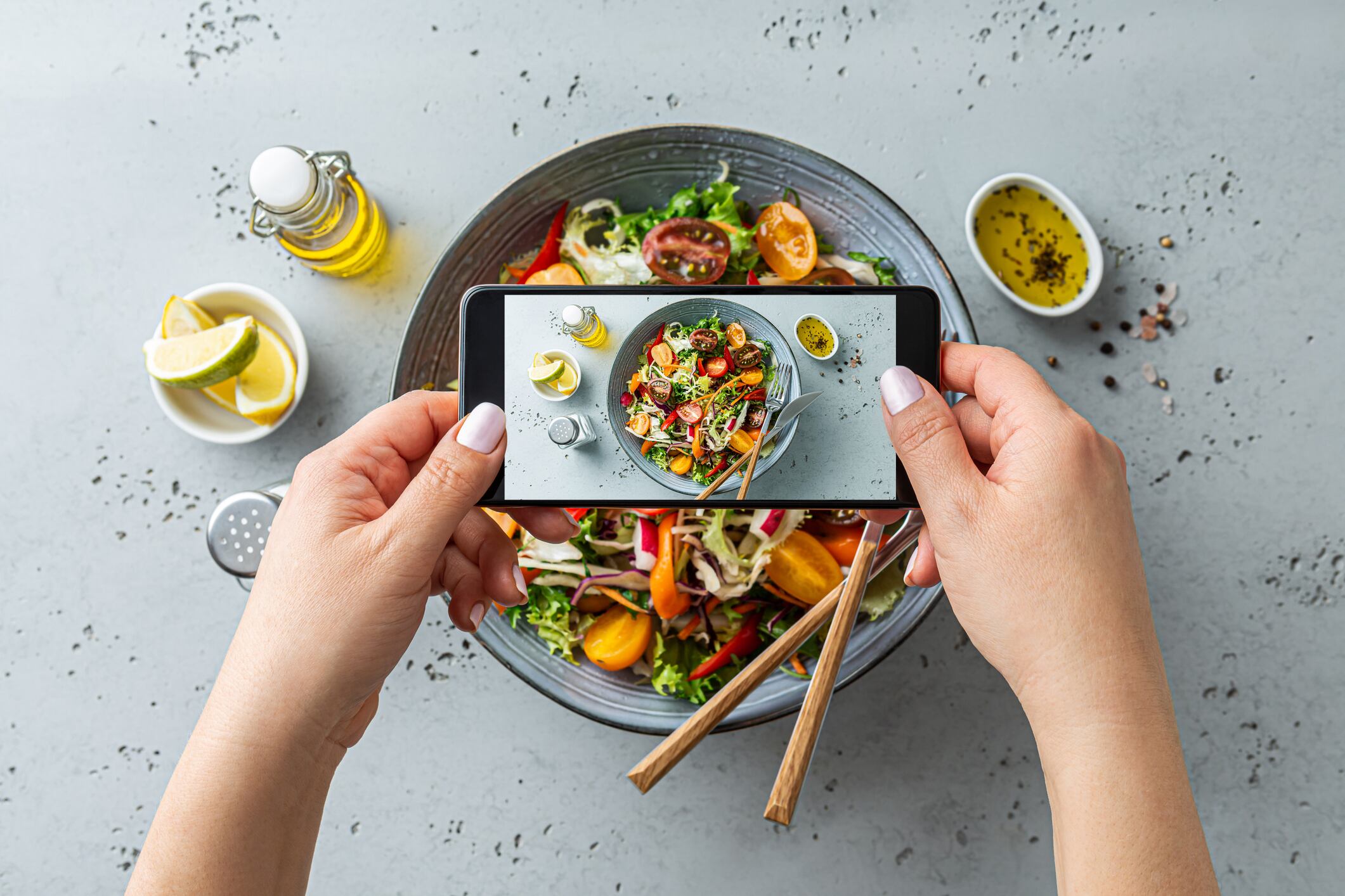 Woman taking photo of fresh, spring, vegetable salad with smartphone. Using phone while eating lunch. Lifestyle trend - posting and sharing food pictures (images) on social media.