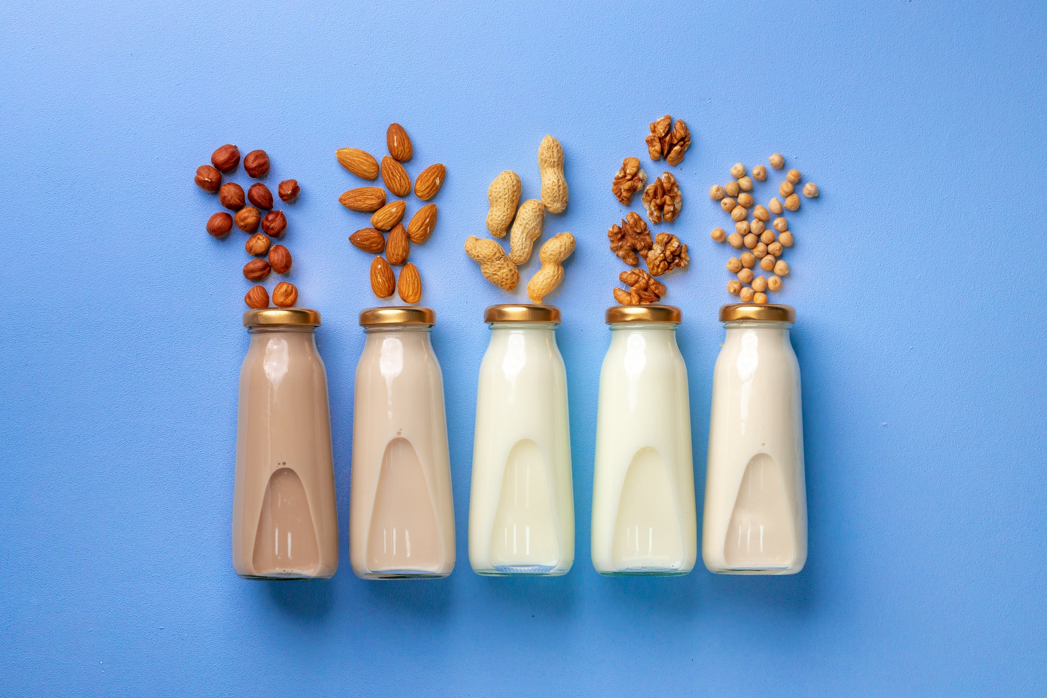 Bottles of vegan non dairy milk with various nuts on blue background, top view