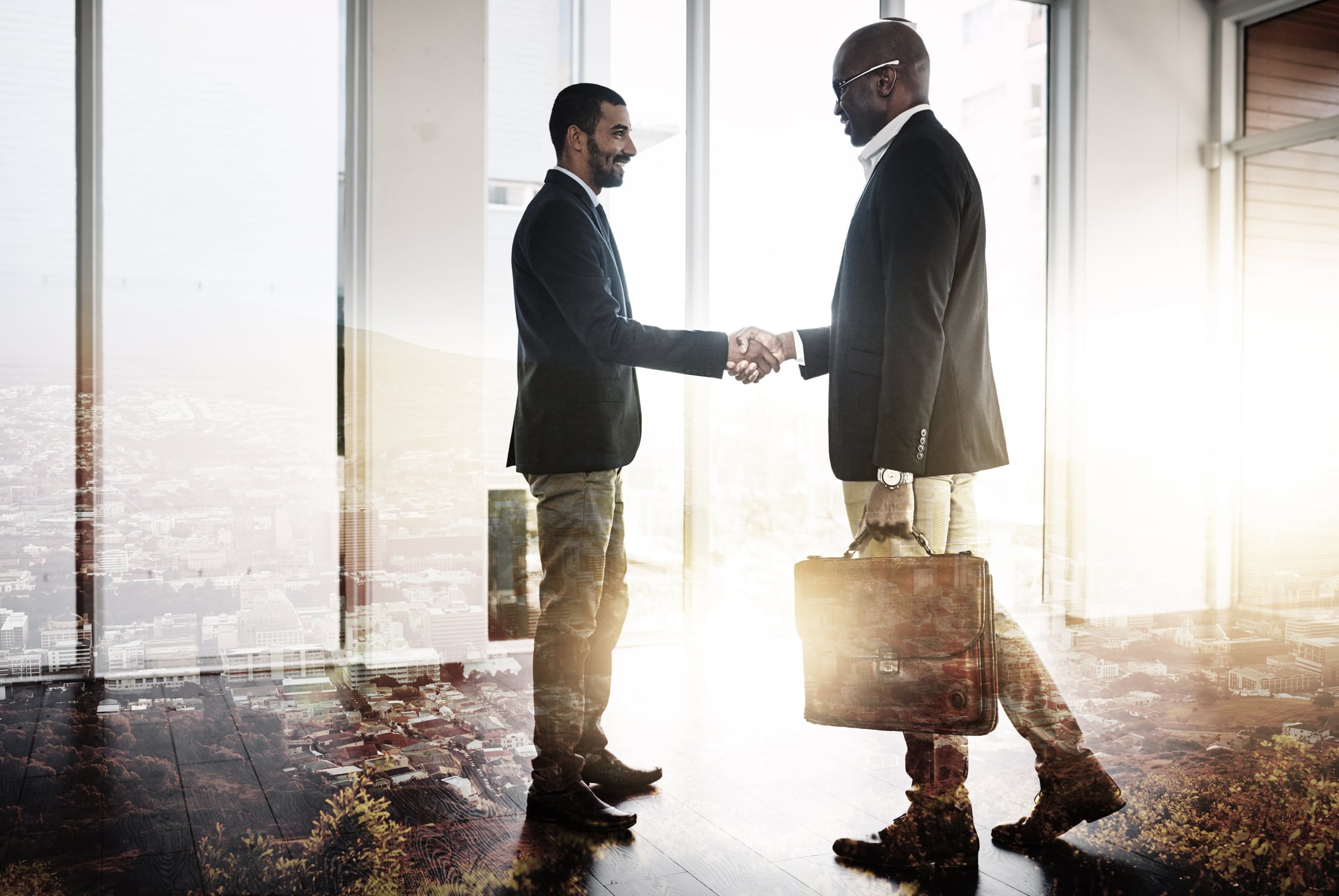 Full length shot of two businessmen shaking hands in an office superimposed over a city background