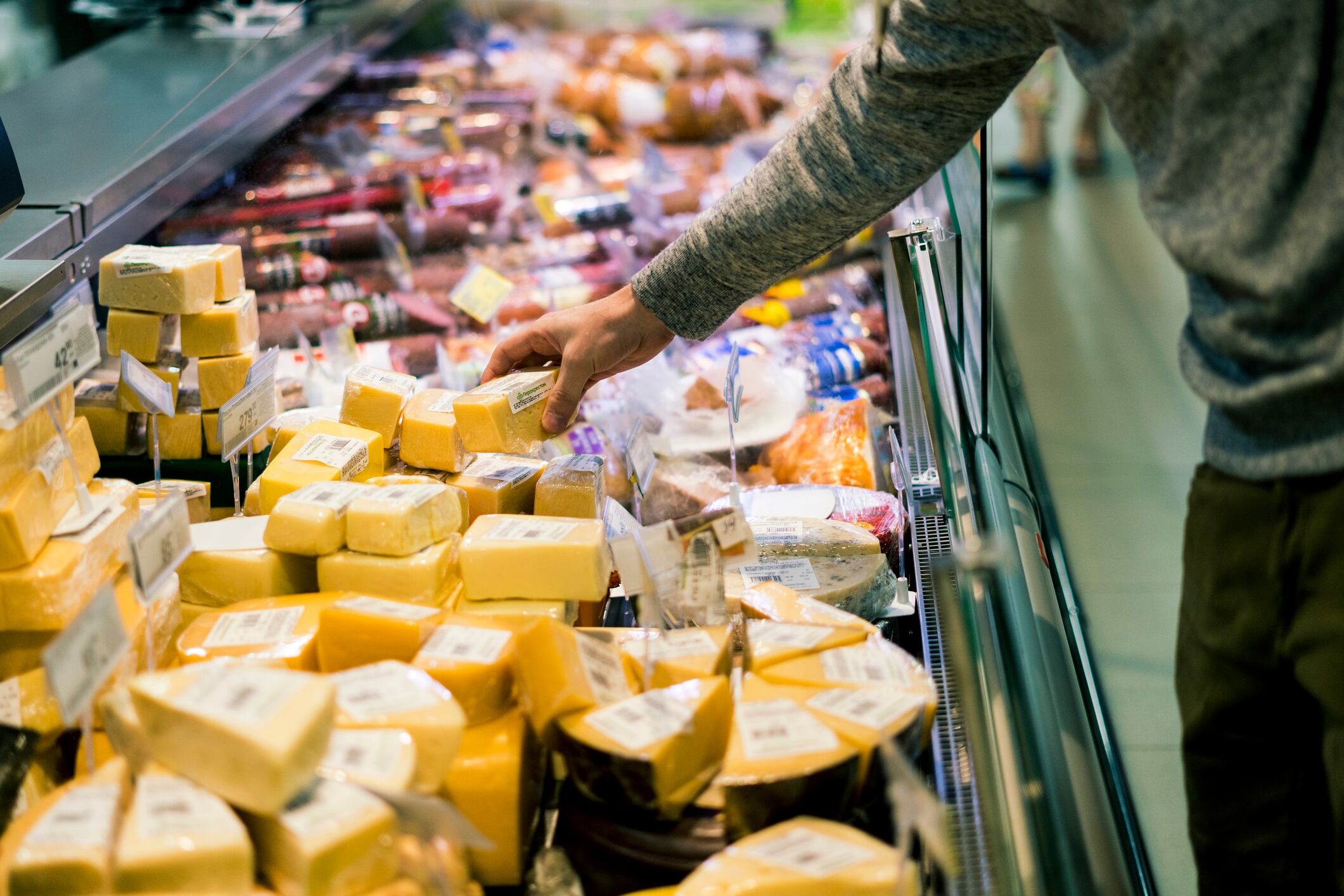 close up person choosing piece of cheese in food shop