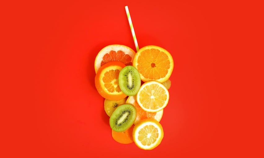 Fruit cup with straw made of pineapple, grapefruit, orange, lemon and kiwi slices against vibrant red background. Copy space. Creative summer idea. Minimal fruit concept.