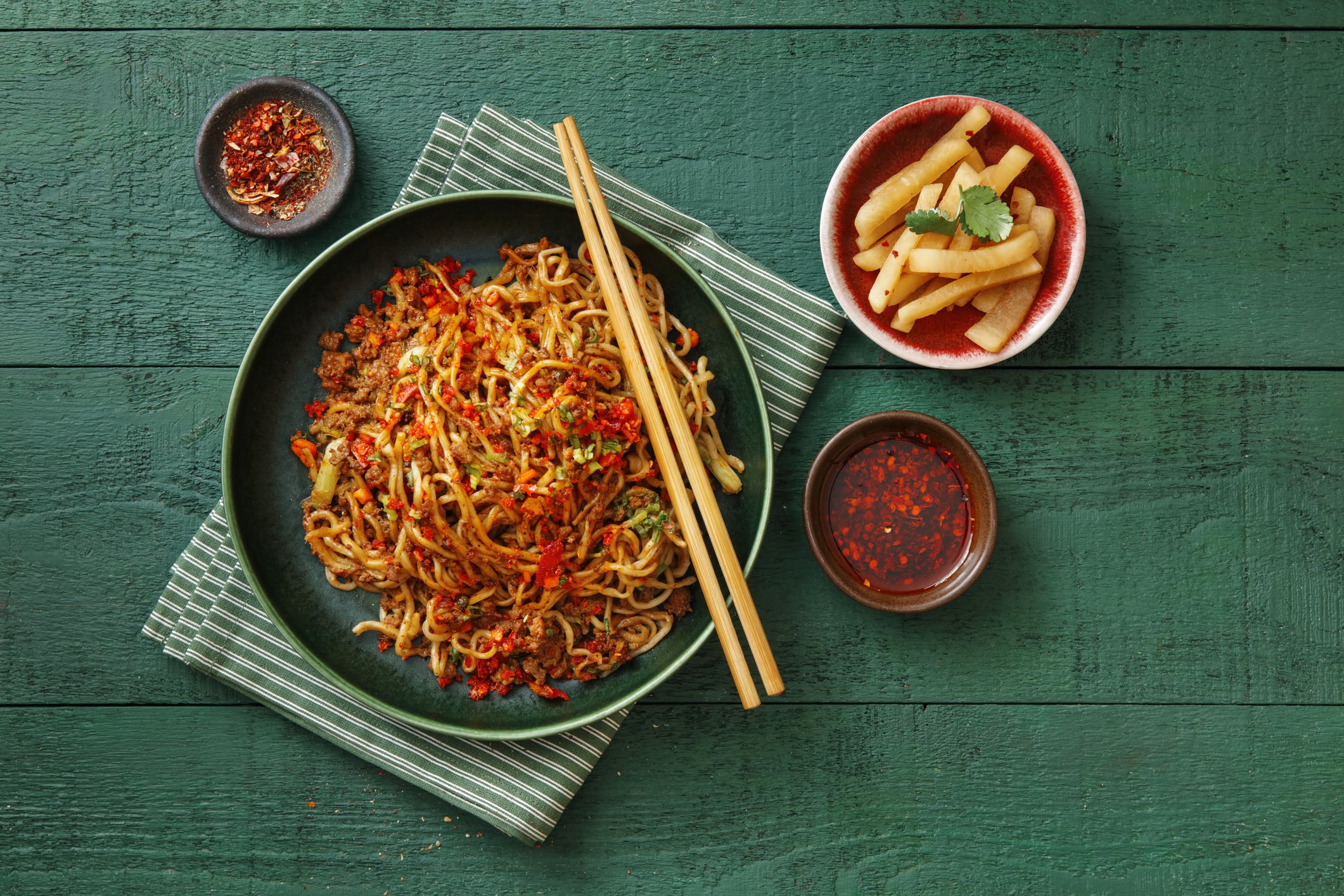 Dandan noodles with spicy sauce, vegetables and minced pork. Flat lay top-down composition on dark green background.