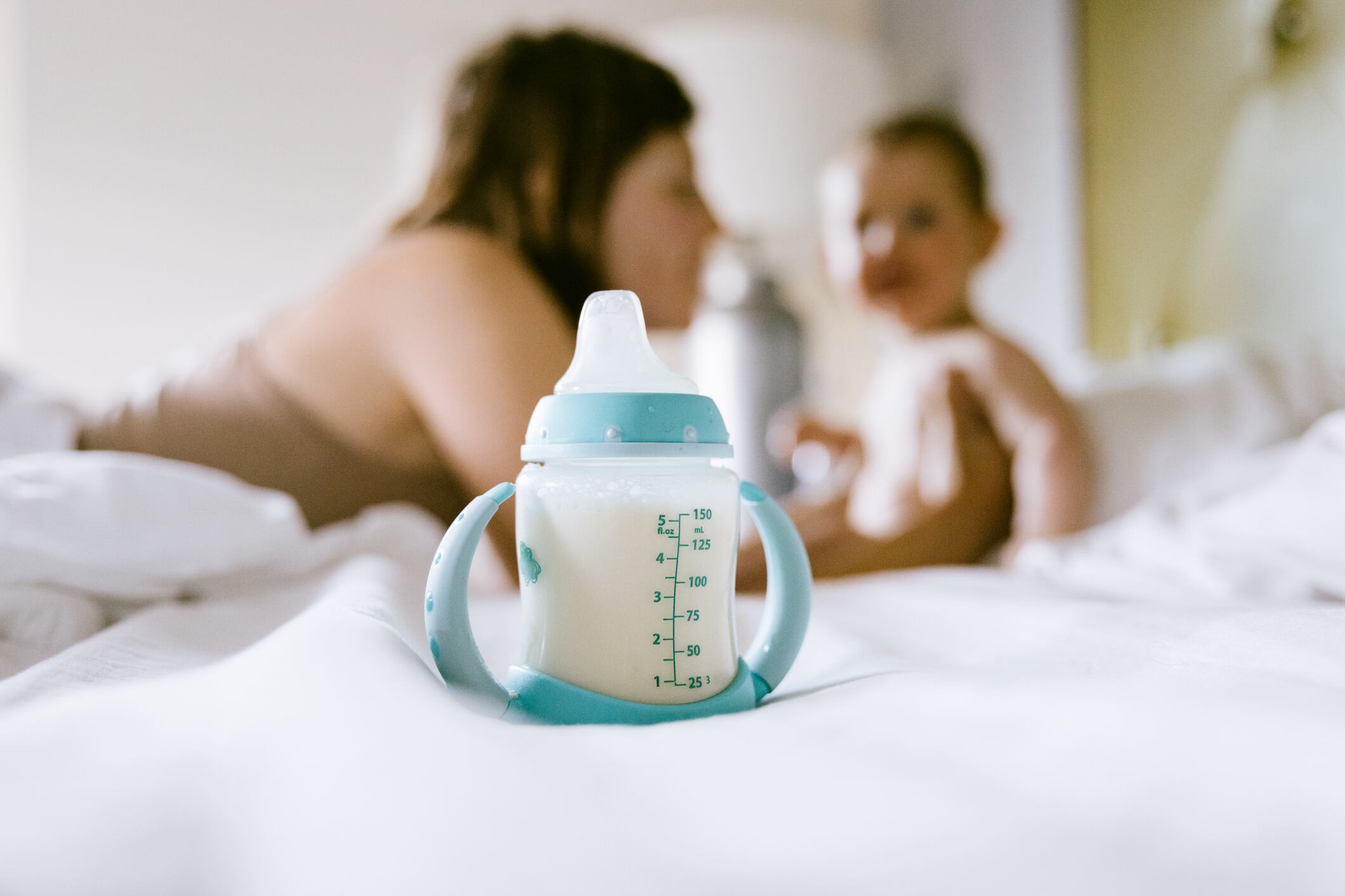A Caucasian mom plays with her baby son, a bottle of baby milk formula in focus in the foreground. Shortages of baby formula have caused food security issues for many families in the United States.
