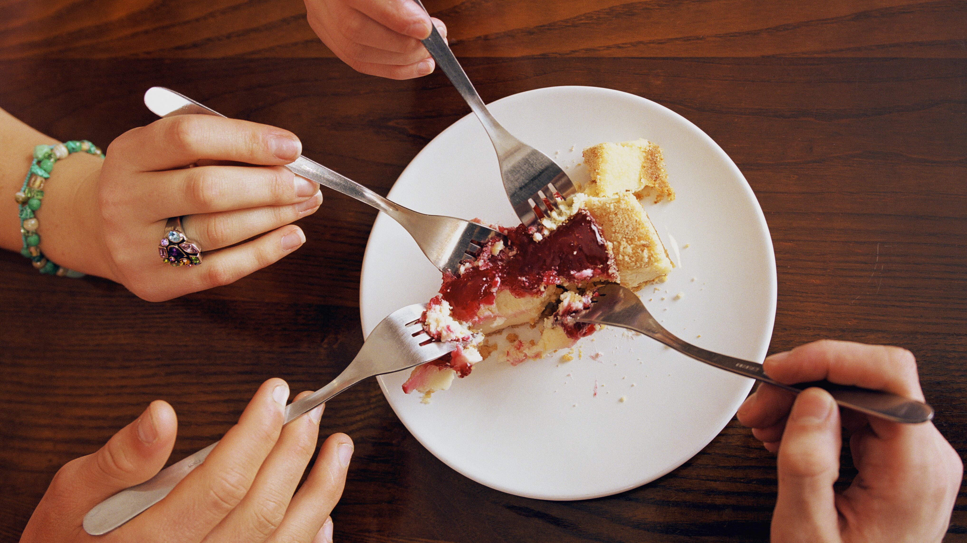 Three teenagers (16-18) and young man sharing cheesecake, close-up