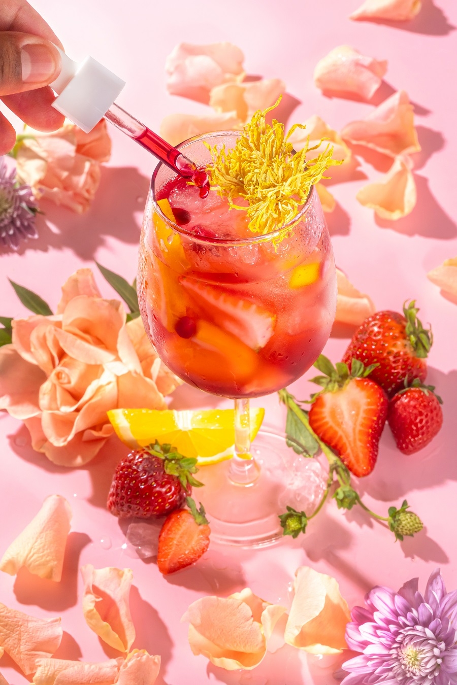 A few drops of Rose Tinted Glasses tincture into a light pink mocktail filled with strawberries and flowers